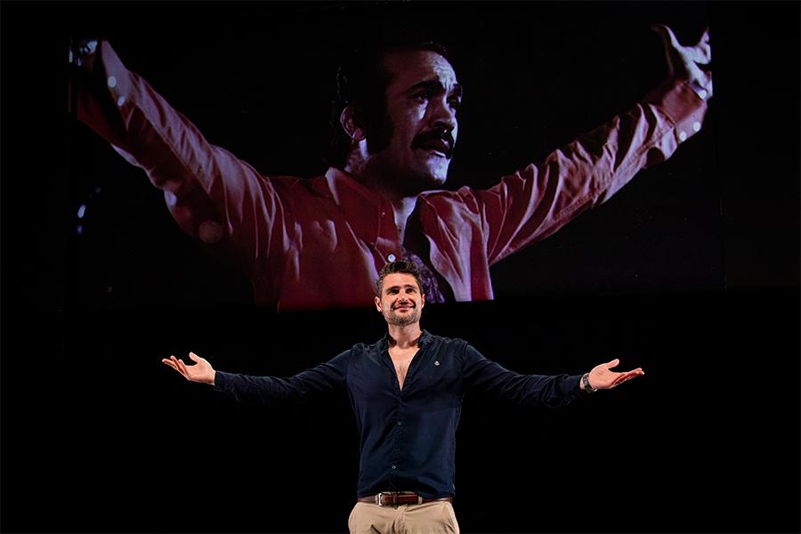 Javaad Alipoor performs on stage with an image of Fereydoun Farrokhzad projected on screen behind him